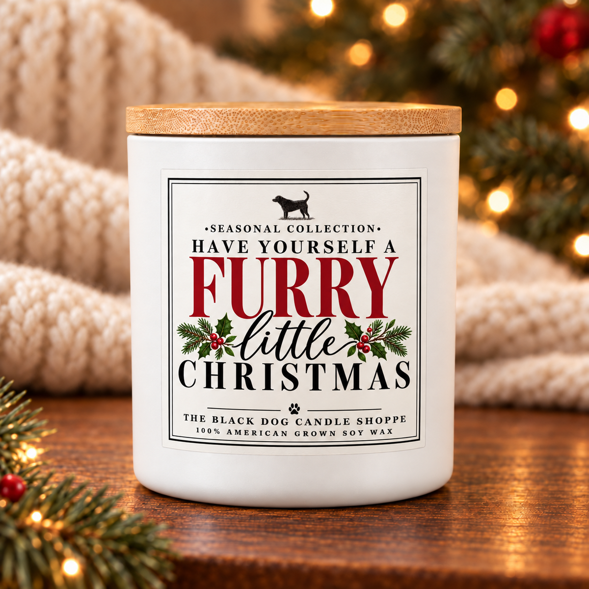 A white scented candle jar with a light wood lid sits on a wooden surface, decorated with a festive Christmas label that reads 'Have Yourself a Furry Little Christmas' and 'The Black Dog Candle Shoppe.' The background features a cozy, warm bokeh of a knitted blanket and a lit Christmas tree.