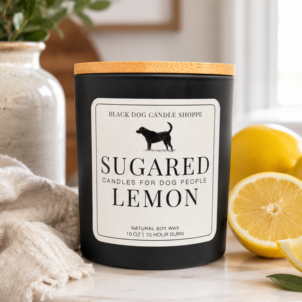 Matte black Sugared Lemon soy candle with bamboo lid displayed on a bright tabletop beside fresh lemons, soft linen, and greenery in a cozy home setting.