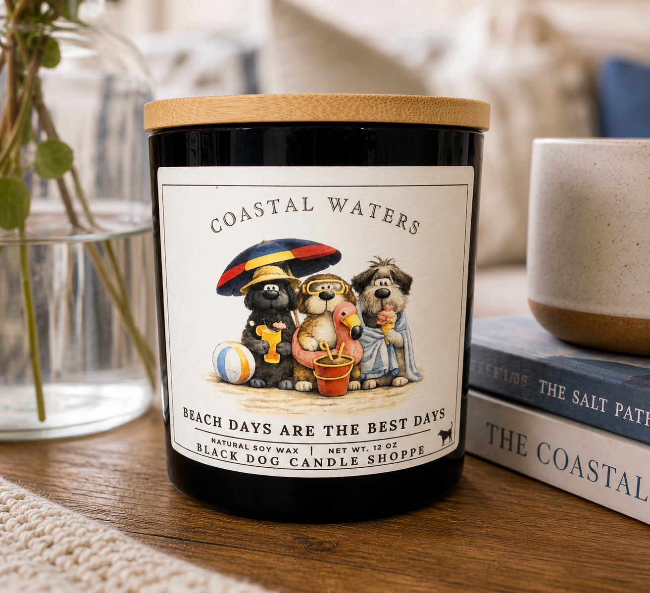 Coastal Waters soy candle in dark blue jar with bamboo lid, featuring dog beach illustration, styled on wooden table with books and greenery