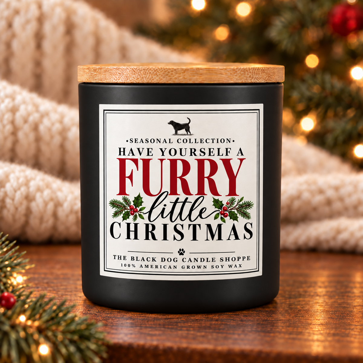 A matte black candle jar with a light wood lid sits on a wooden surface, surrounded by cozy holiday decor including pine branches, warm string lights, and a knitted blanket. The front label reads 'HAVE YOURSELF A FURRY little CHRISTMAS' with holly and dog silhouette graphics.
