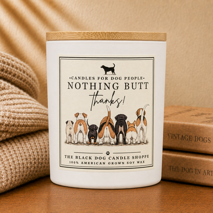 A white candle jar with a bamboo lid sits on a wooden surface, styled with a beige knit blanket on the left and vintage-style dog books on the right. The front label reads 'NOTHING BUT THANKS!' and shows several dog illustrations.